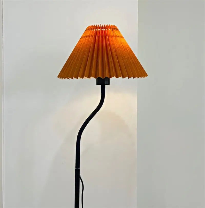 Warm yellow pleated fabric lampshade on black floor lamp in cozy room