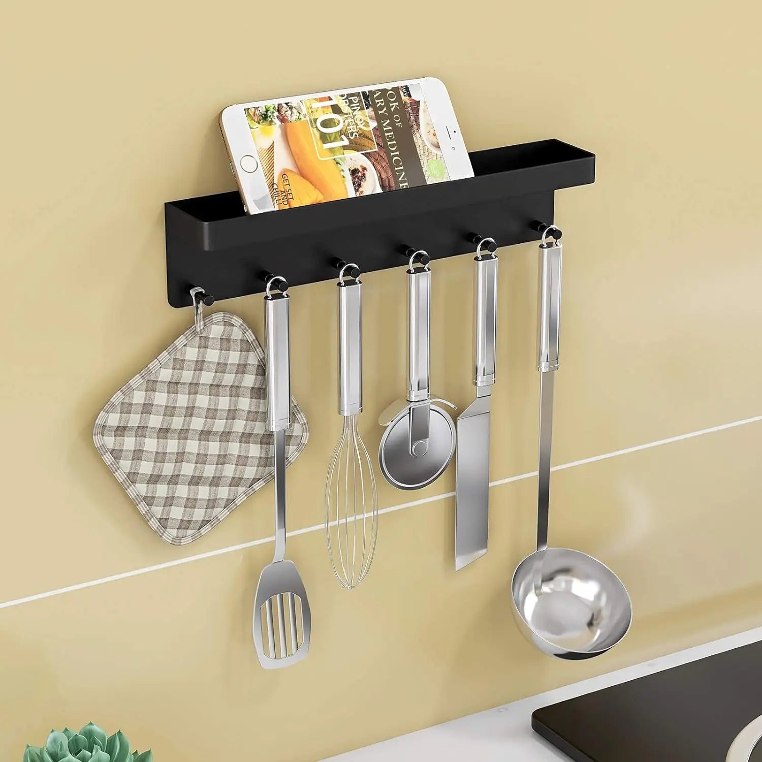 Black wall-mounted organizer with utensils and kitchen tools hanging from hooks, phone in tray