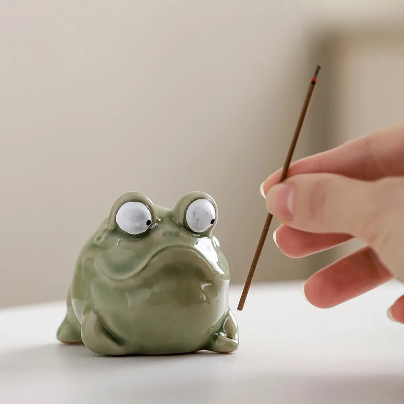 Hand placing incense stick in a ceramic frog incense holder