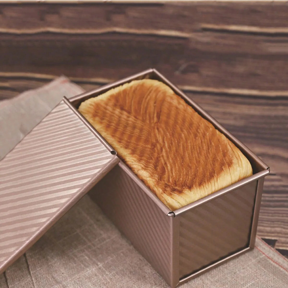 Golden rectangular bread box with lid partially removed, on linen cloth