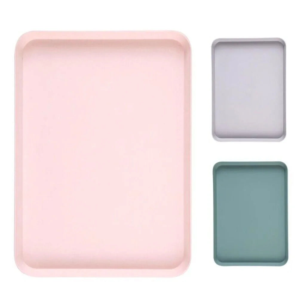 Top-down view of three matte rectangular trays in pink, gray-purple, and green, demonstrating size options.