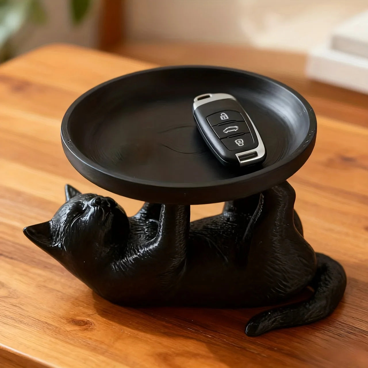 Empty black cat jewelry tray with a car key on a wooden table