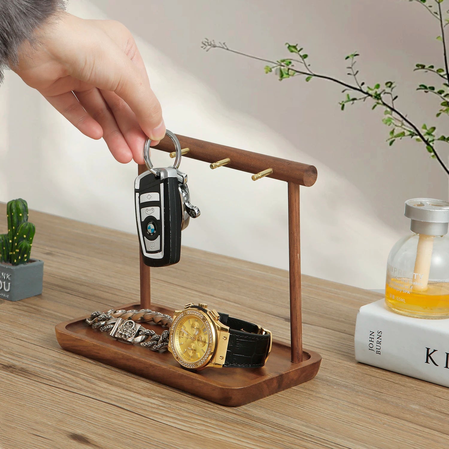 Hand placing key on hook of walnut and metal jewelry stand with watch and bracelet displayed in tray