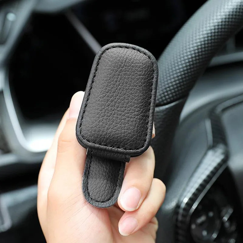 Hand holding a black PU leather glasses holder clip inside a car