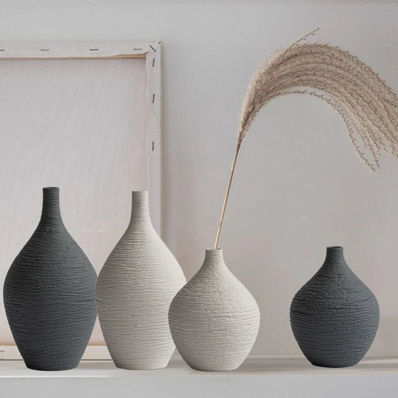 Four textured ceramic vases in beige and grey lined up on a shelf with a decorative dried stem