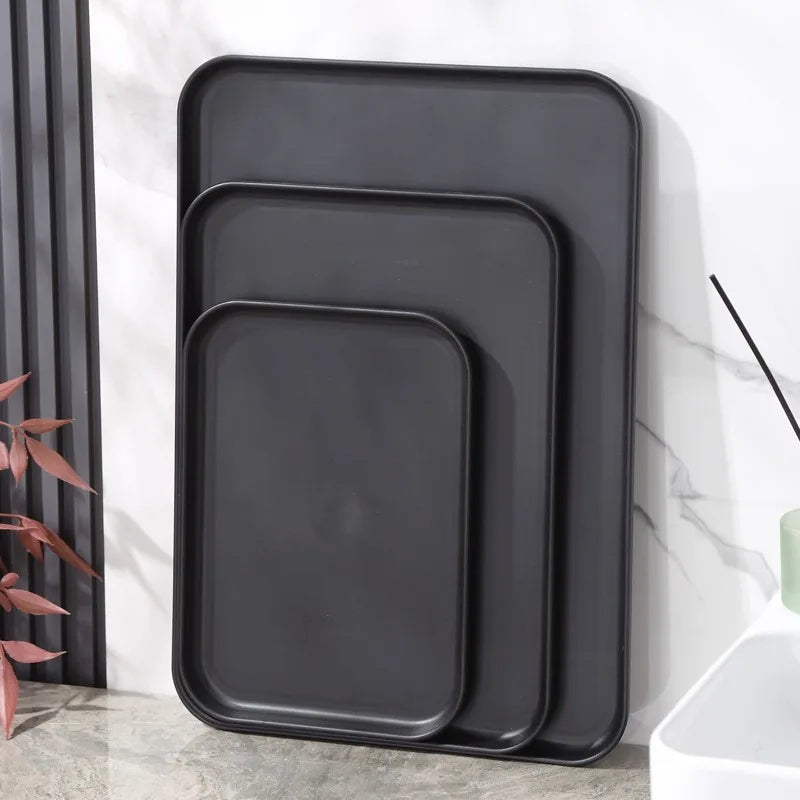 Set of three matte black rectangular plastic non-slip trays stacked upright on a countertop