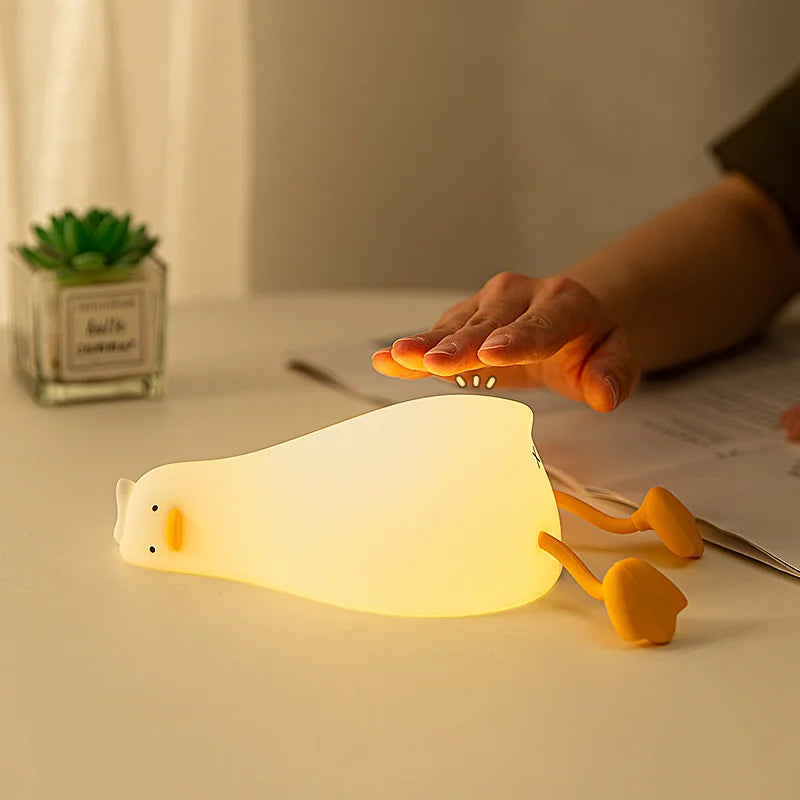 Duck silicone night light glowing on a bedside table with a hand reaching over