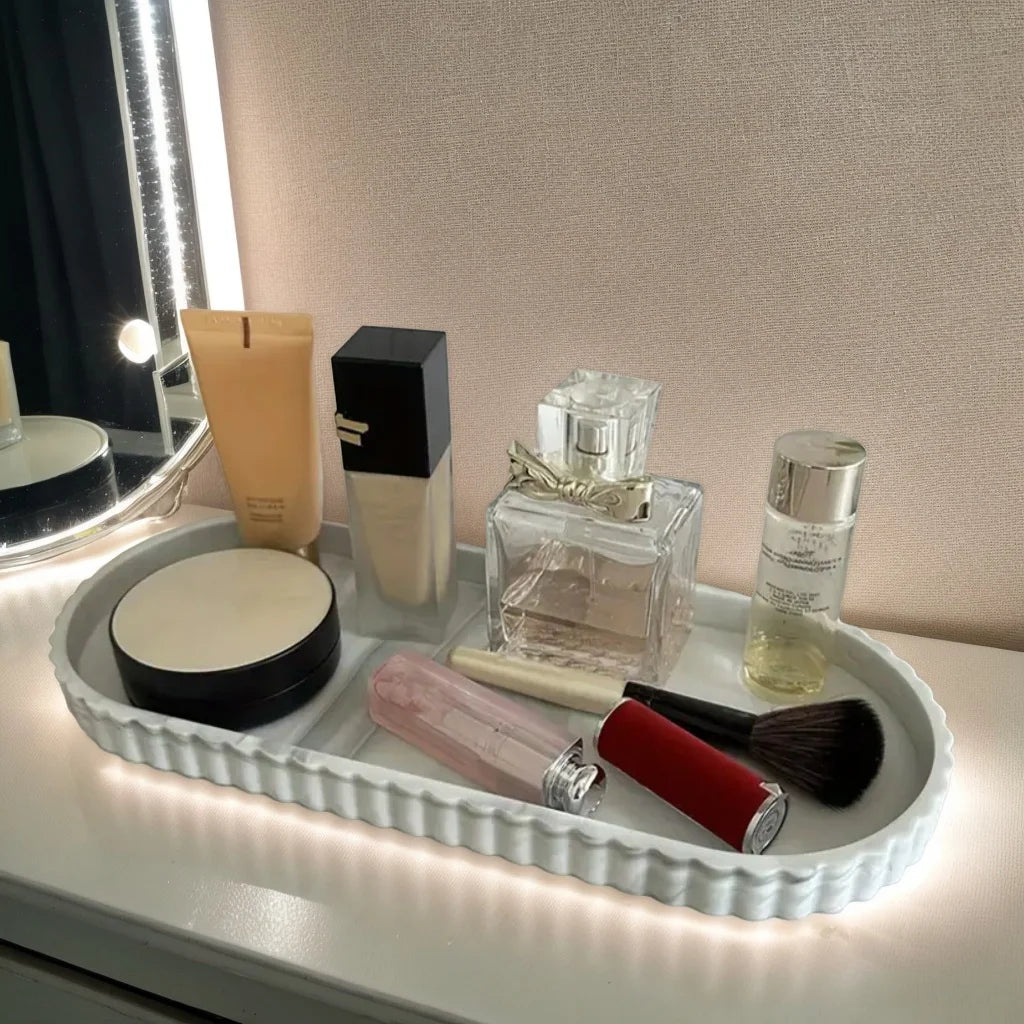 White marble-patterned oval silicone tray with everyday toiletries, styled on a vanity with lighting