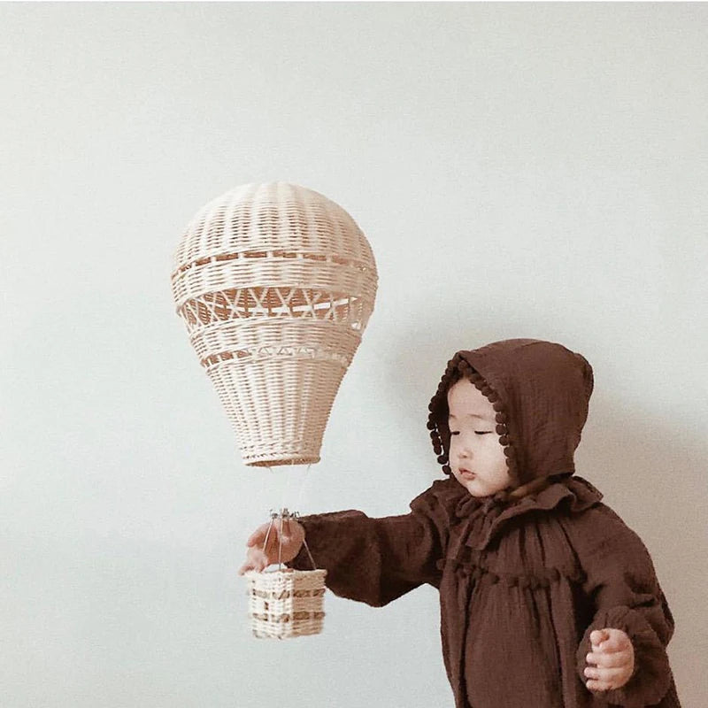 child reaching toward hand-woven rattan hot air balloon wall hanging