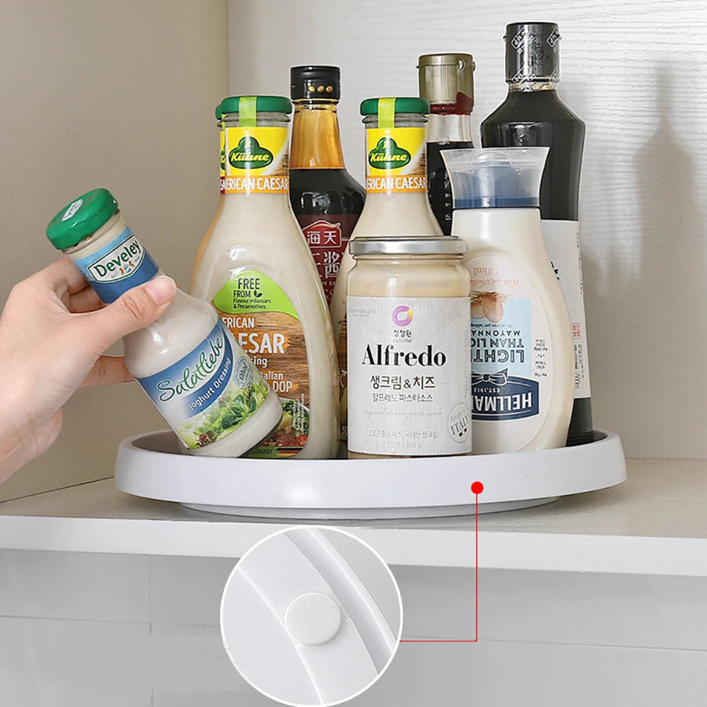 Hand spinning a white and gray rotating turntable organizer holding bottles in a kitchen cabinet