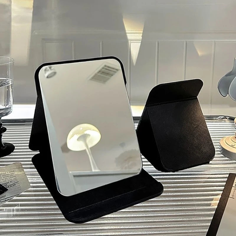 Two standing foldable black PU leather mirrors on a desk, showing the mirror's back and front.