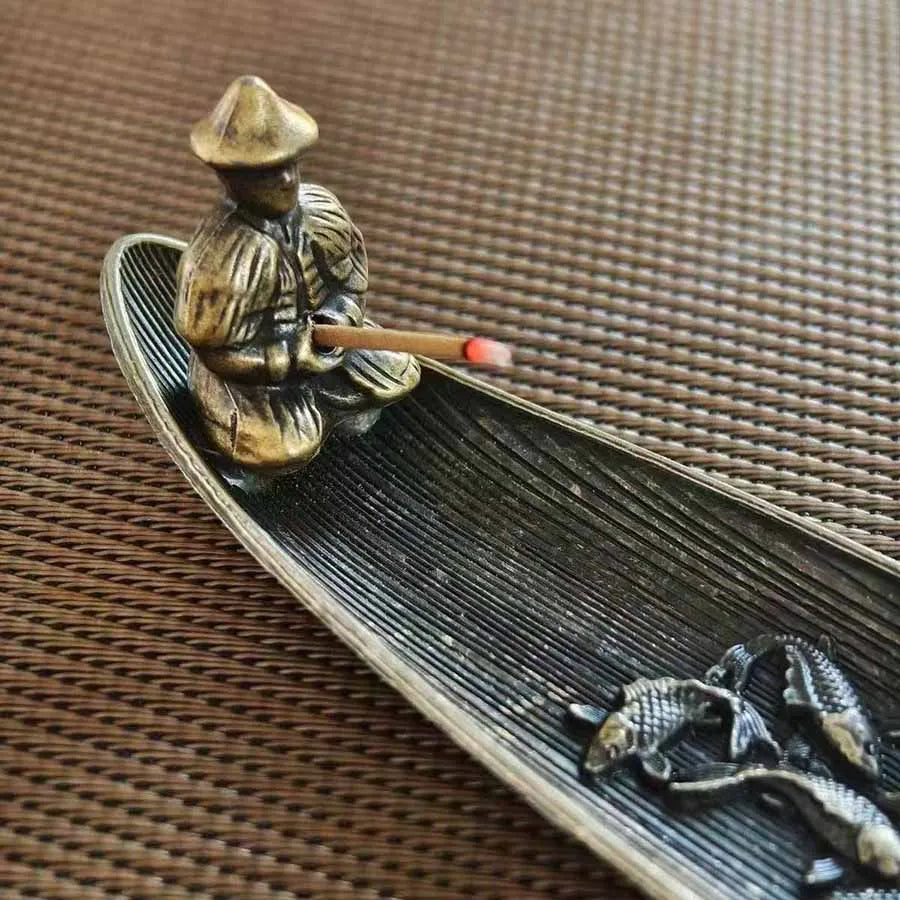 Close-up detail of the seated figure on boat-shaped metal incense holder