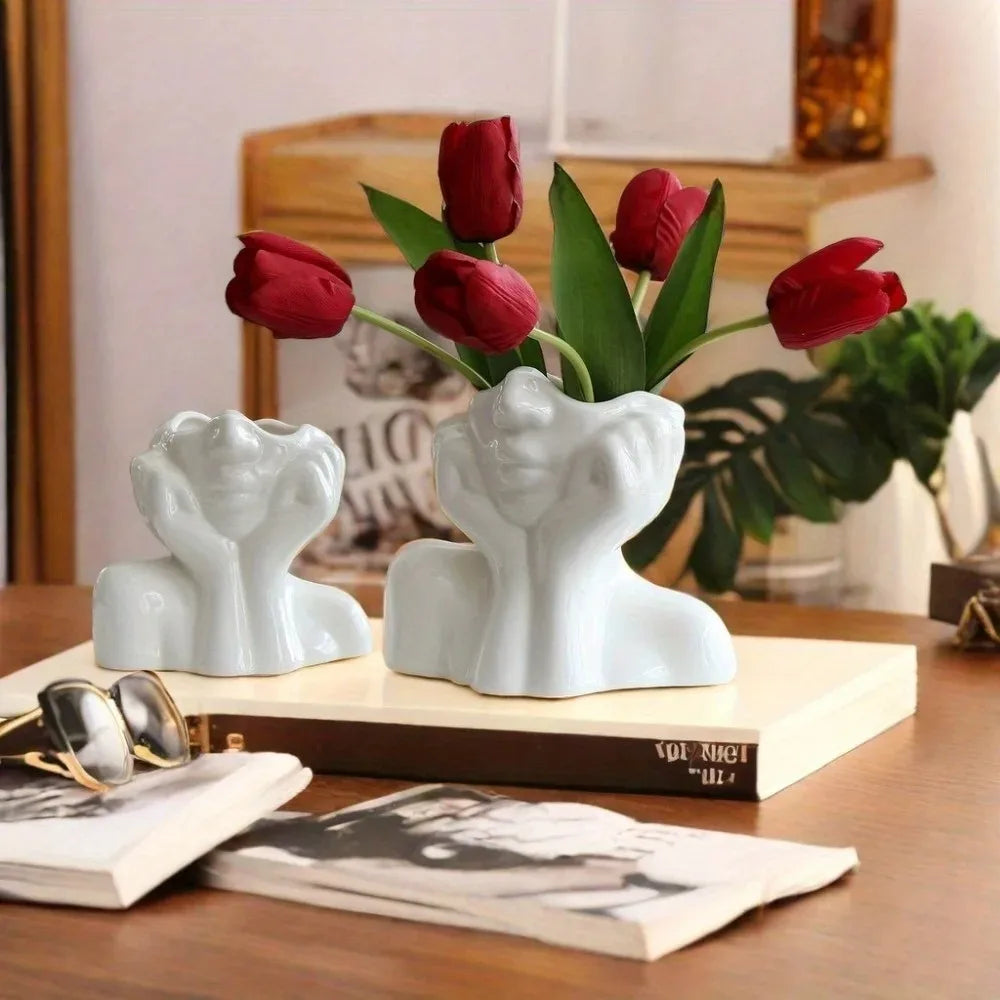 Two face sculpture holders used as vases with red tulips on a wooden table