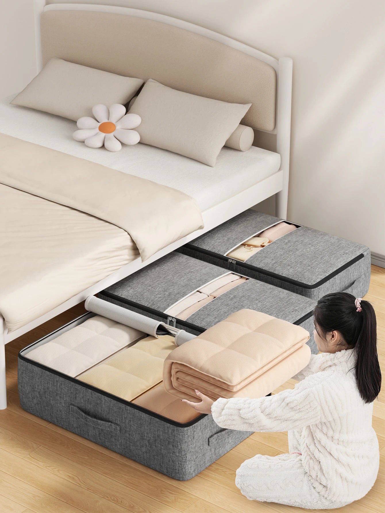 Two grey foldable underbed storage bags filled with blankets and clothing, being packed under a bed