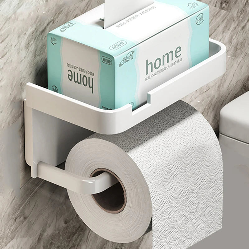 Wall-mounted white toilet paper holder with top tray holding a tissue box, installed next to a toilet.