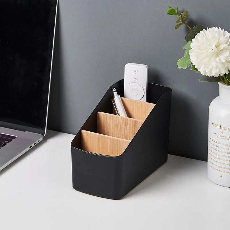 Black remote organizer with bamboo dividers on a modern desk, storing a remote and pen