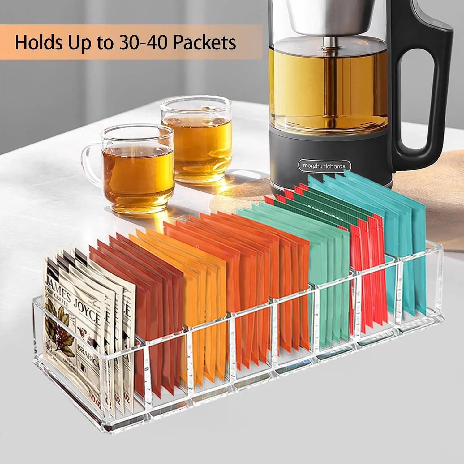 Acrylic tea bag holder on a kitchen counter near tea cups and a tea maker.