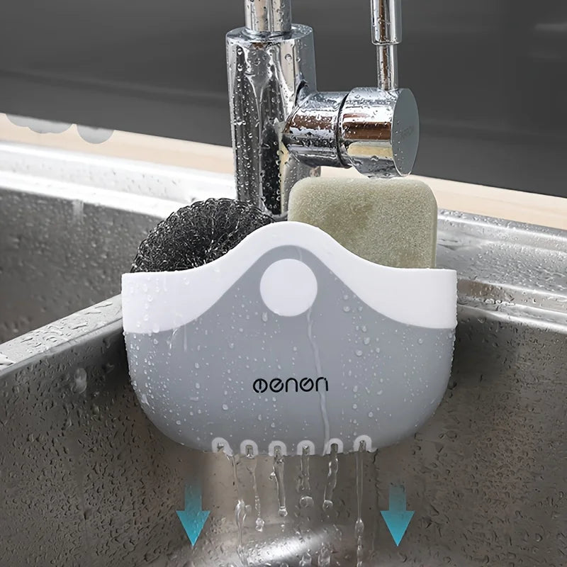 Gray sink caddy basket hanging from a kitchen faucet holding sponge and scrubber, water draining below