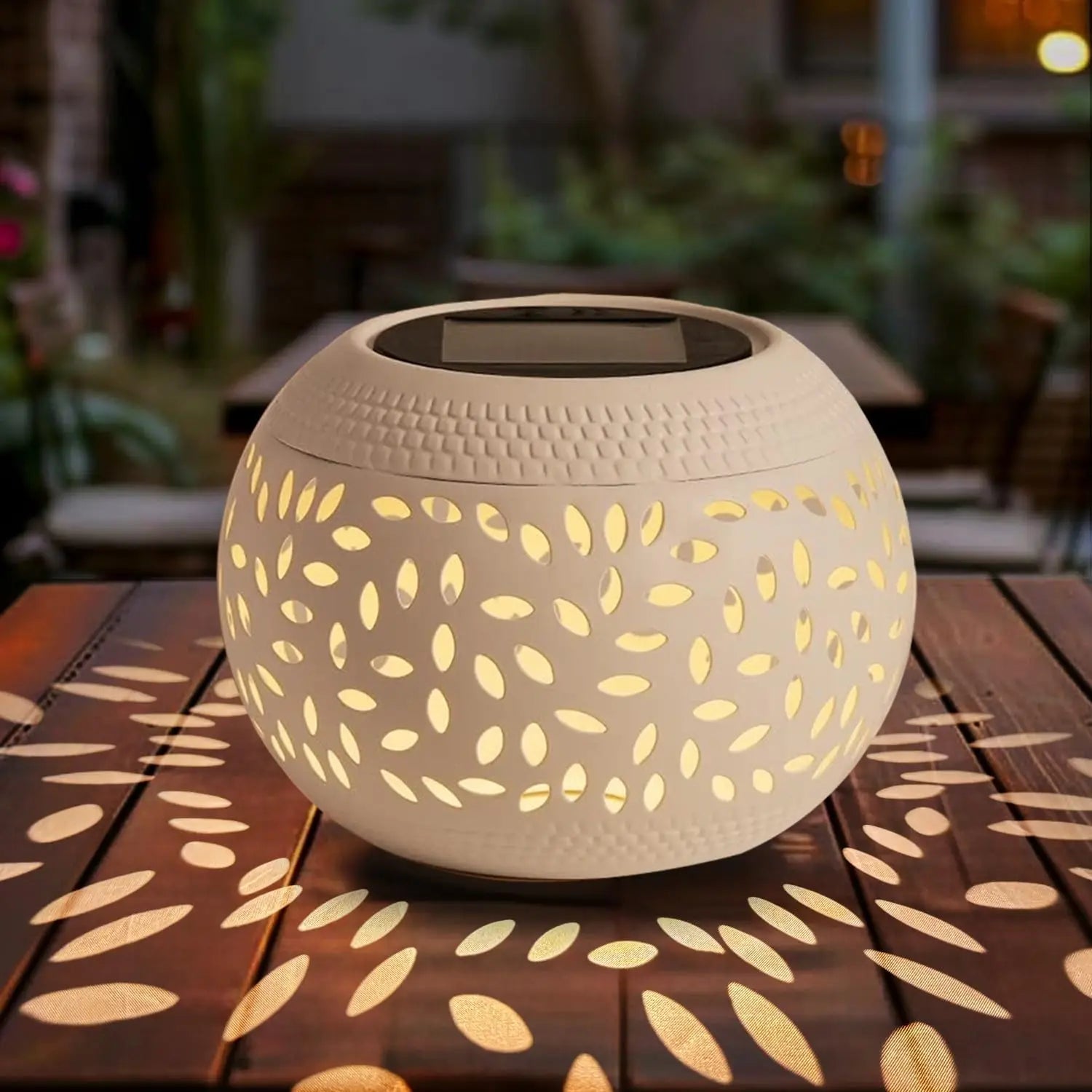 White hollowed solar table lantern casting warm patterns on an outdoor table