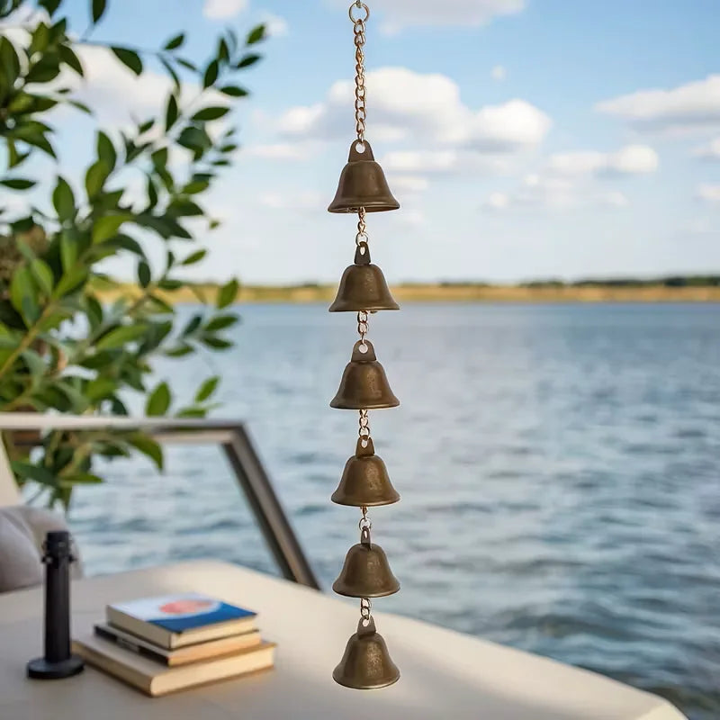 Iron bell wind chime hanging on a porch with water and books in the background