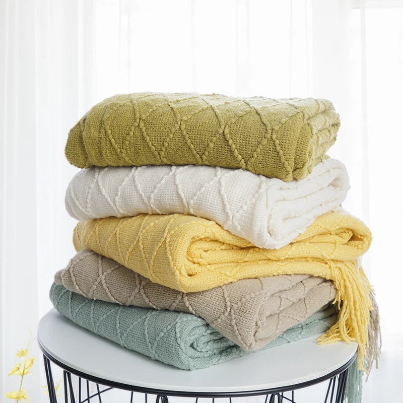 Stacked plaid knit throw blankets in yellow, white, beige, and sage green on a round table