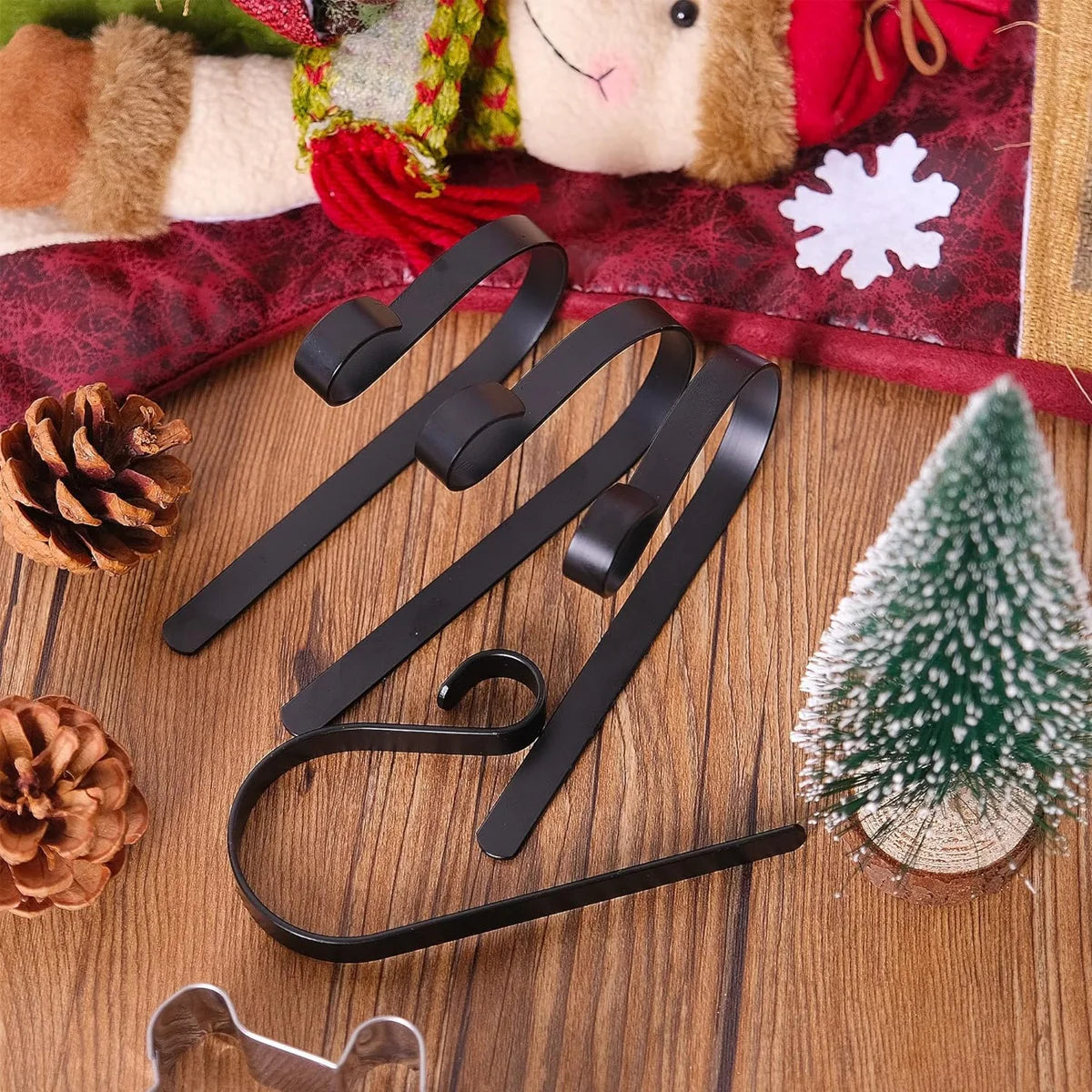 Black stainless steel stocking holders displayed on a wood surface with pinecones and festive decor