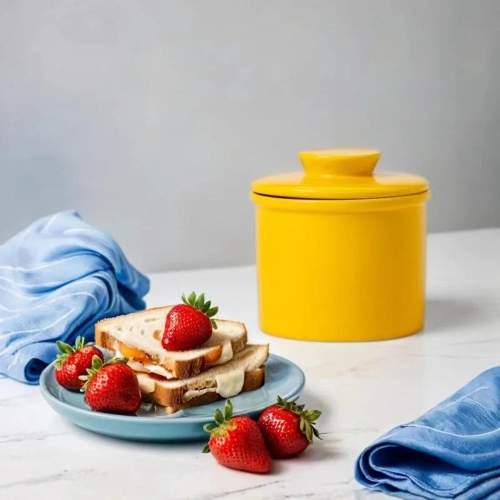 Yellow ceramic butter crock with lid next to a plate of strawberry sandwiches