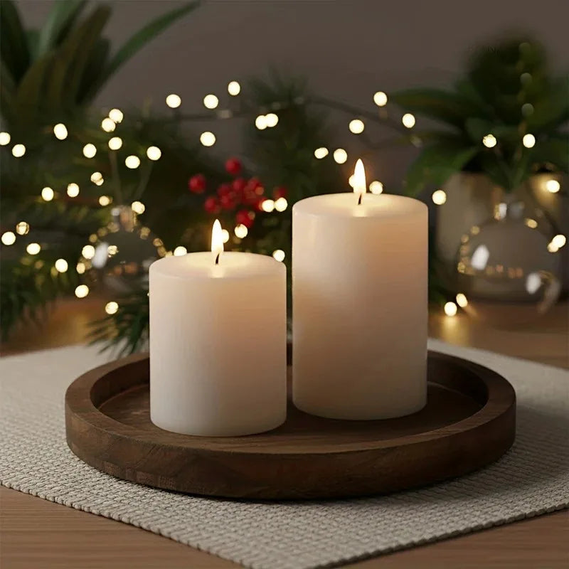 Small round wood tray with two pillar candles, on a woven placemat with festive lights and greenery in background