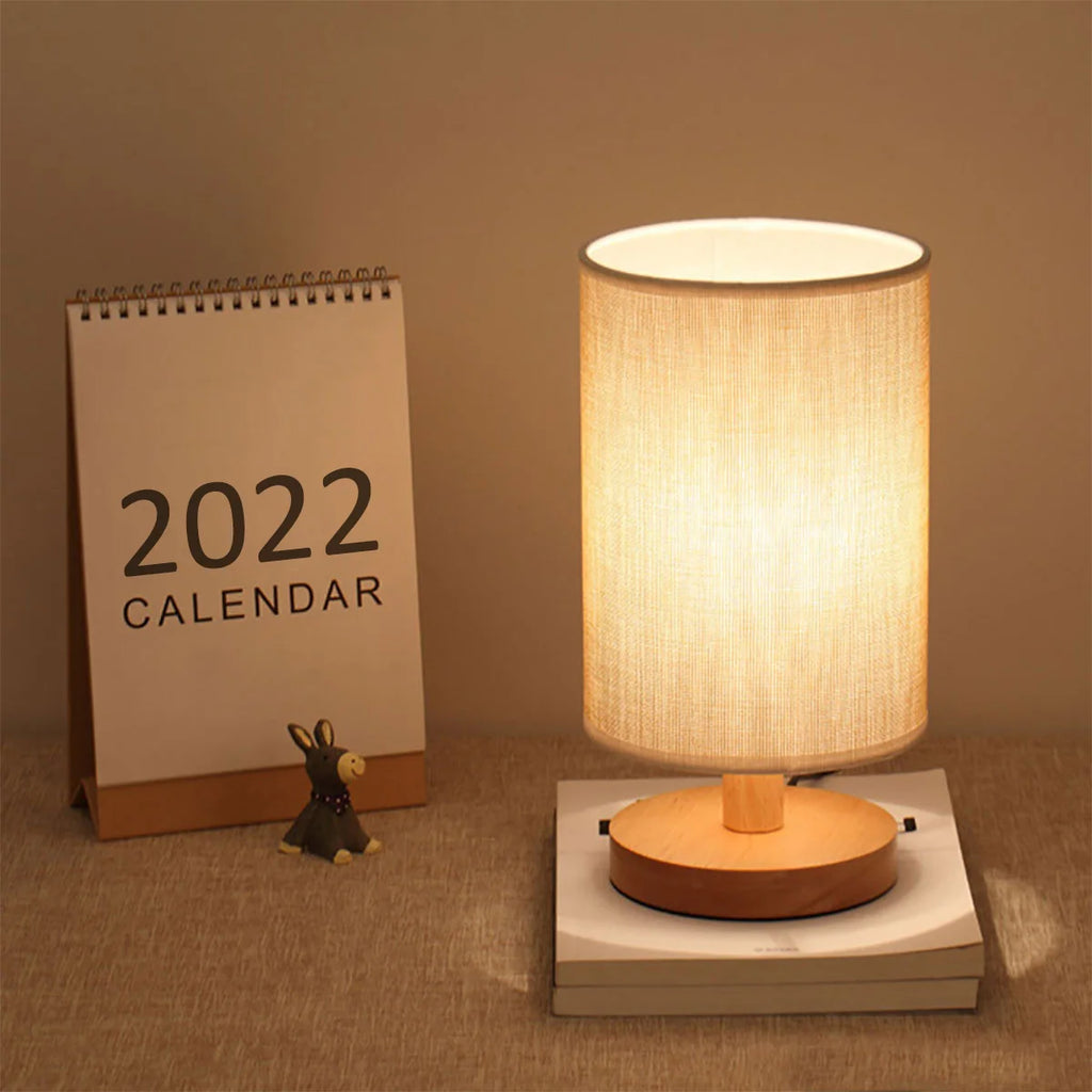 Cylinder table lamp with linen shade on a desk beside a standing calendar
