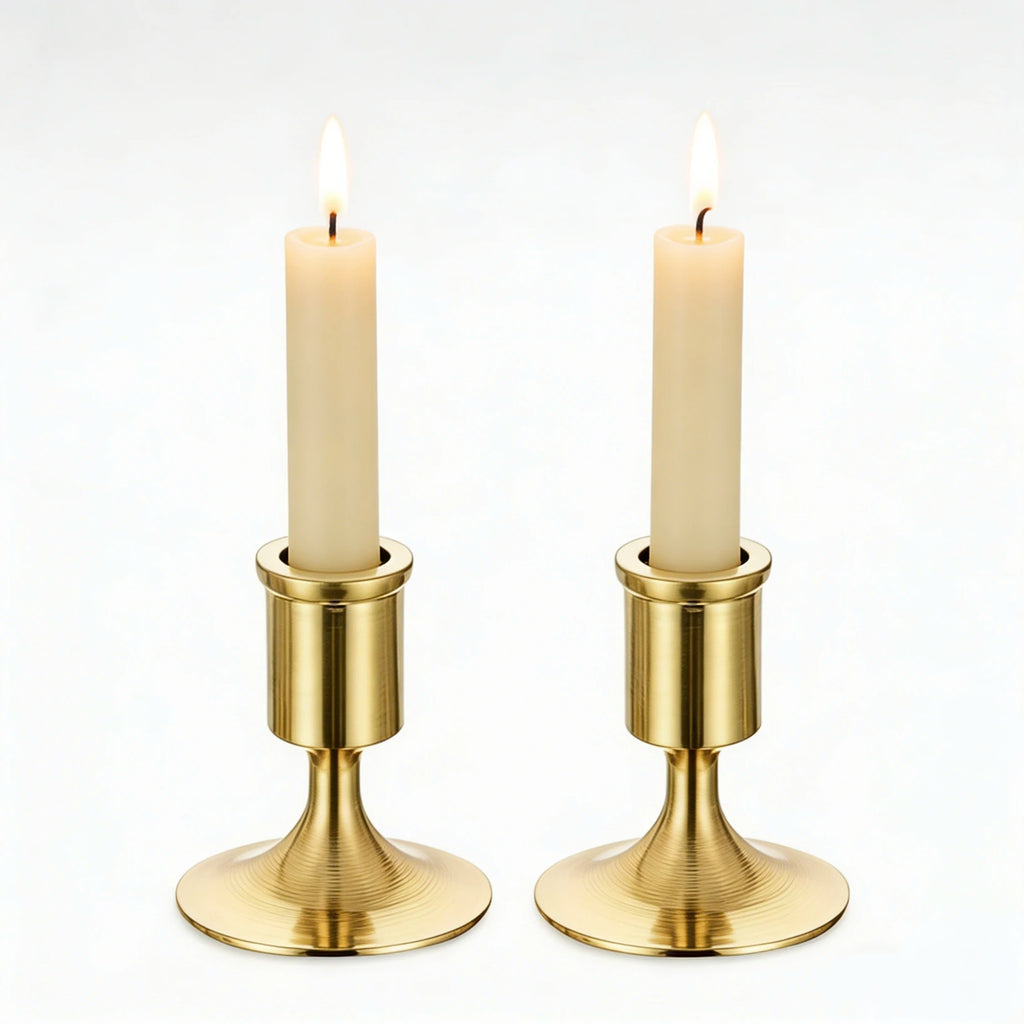 pair of gold brushed metal taper candle holders with lit candles on white background