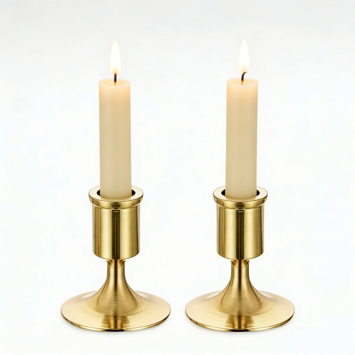 pair of gold brushed metal taper candle holders with lit candles on white background