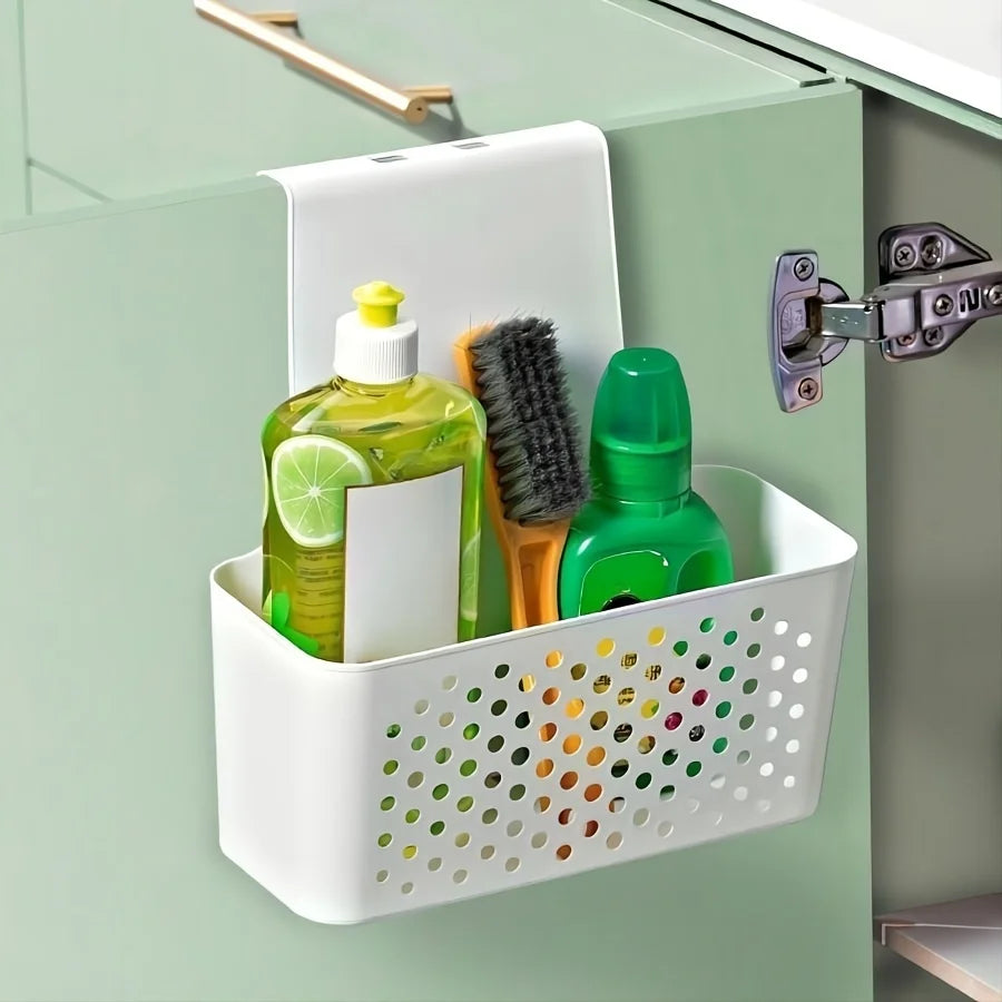 White plastic cabinet door basket hanging inside a green kitchen cabinet, holding cleaning supplies including a dish soap bottle, brush, and cleaner.