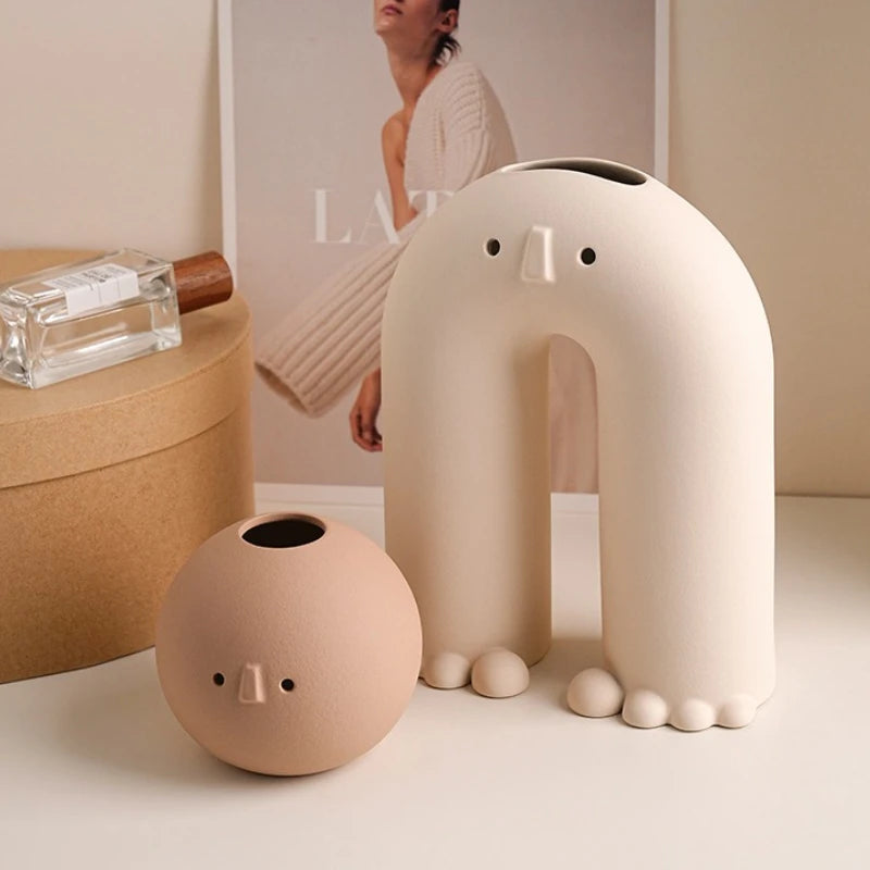 White arch-shaped ceramic face vase and round beige vase on a tabletop near minimal decor