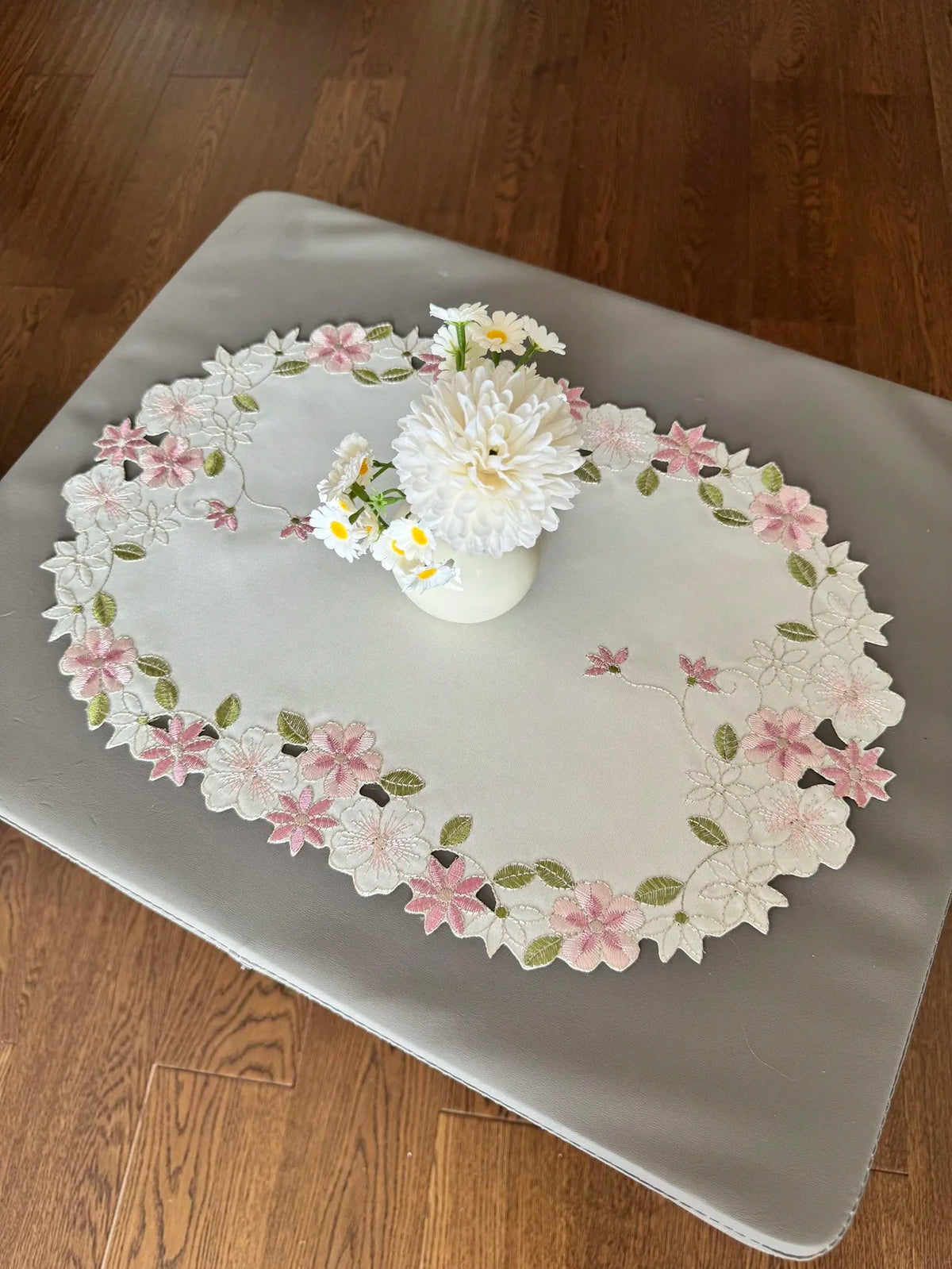 Round floral embroidered placemat, 30cm diameter with pink and white flowers and green leaves, on textured surface