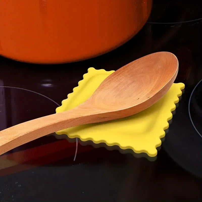 Wooden spoon resting on a yellow biscuit-shaped silicone spoon rest on a dark stovetop