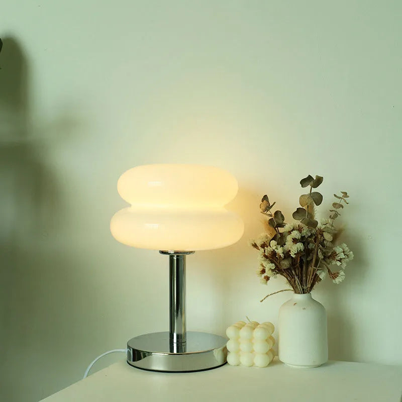 White glass macaron table lamp softly glowing in a bedroom setup