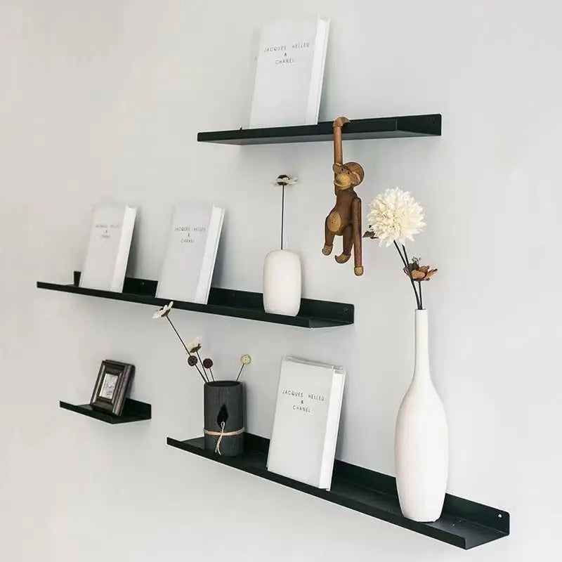 Black metal wall-mounted picture ledge shelves holding books, vases, and decor on a white wall