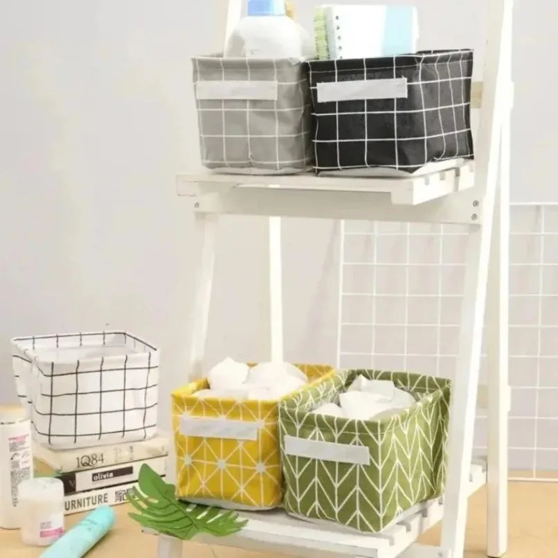 Fabric storage baskets in grey, black, white, yellow, and green patterns on a white shelving unit, holding toiletries and notebooks.