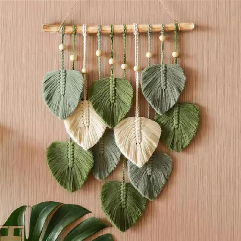 Close-up of hand-woven leaf macrame wall hanging in green and cream against a tan wall