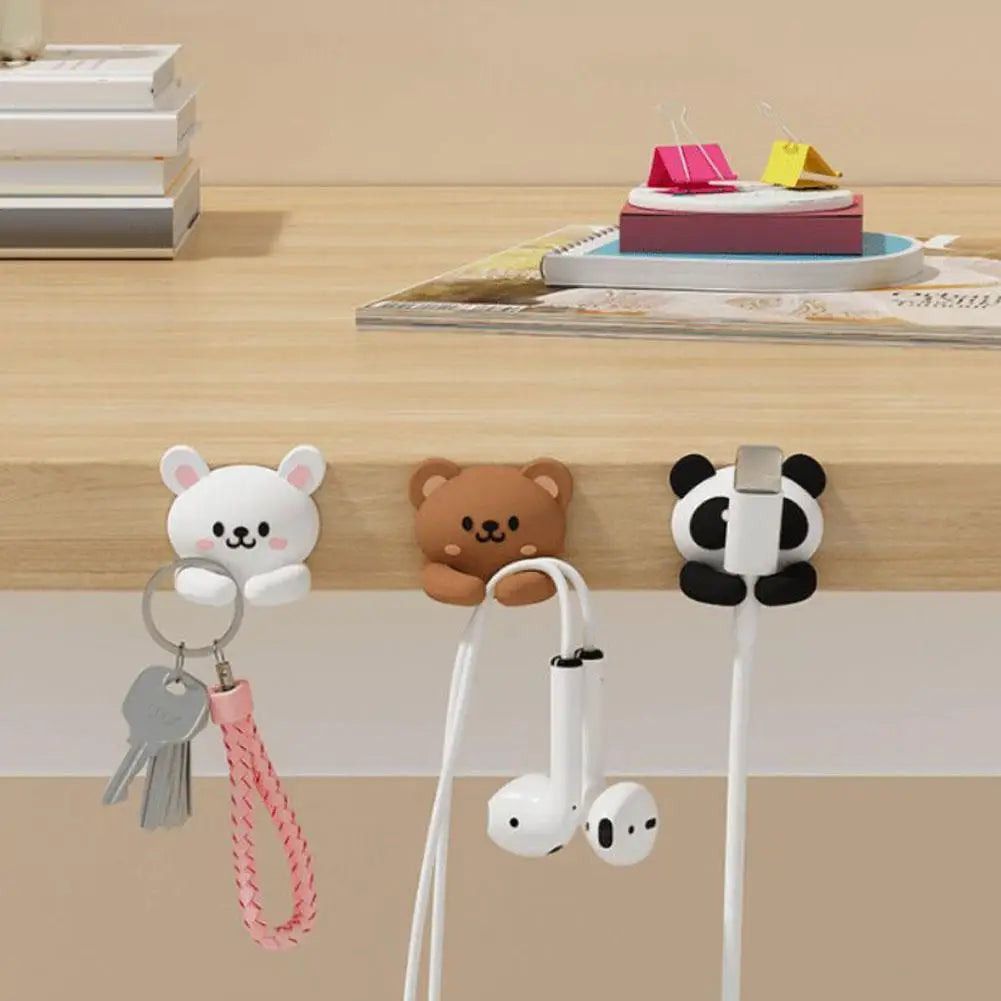 Three animal-shaped cable clips, rabbit, bear, and panda, holding keys and cables on the edge of a desk