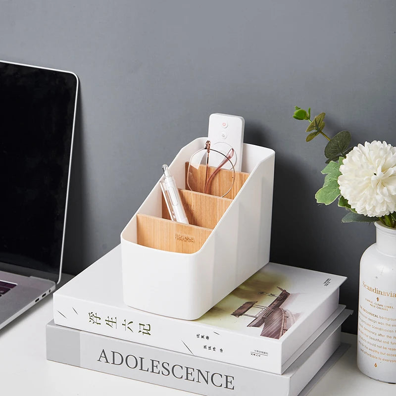 White organizer with bamboo dividers on stacked books beside a laptop, holding a remote, glasses, and pen