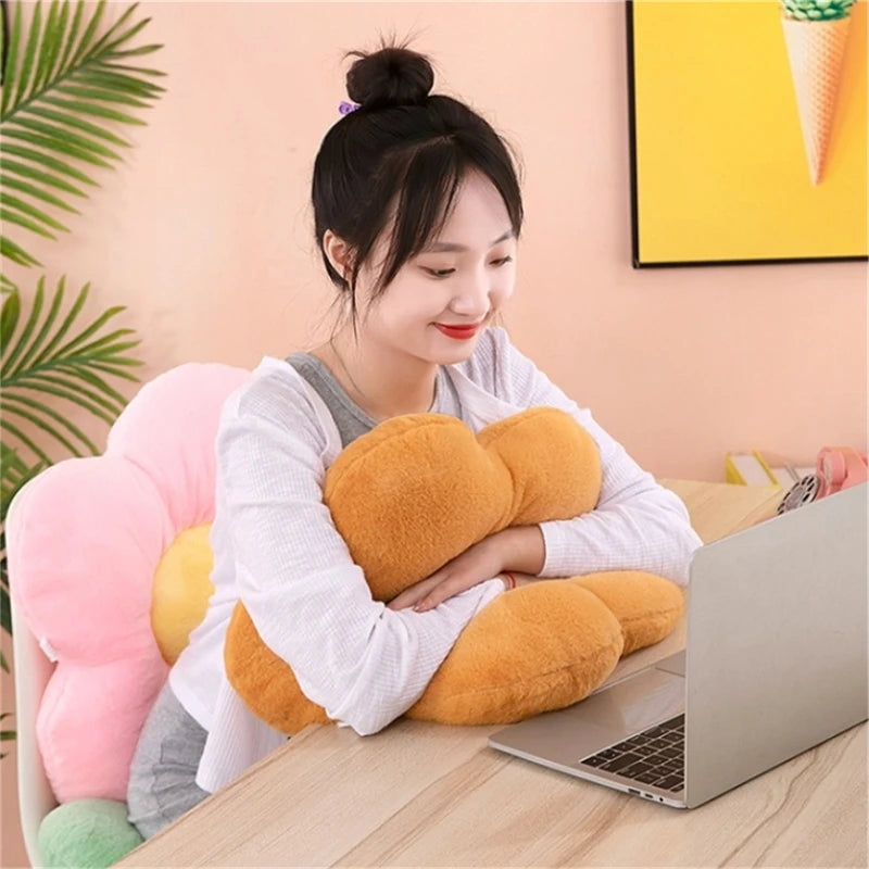 Person sitting at a desk hugging a tan plush flower cushion with a pink cushion as chair back support