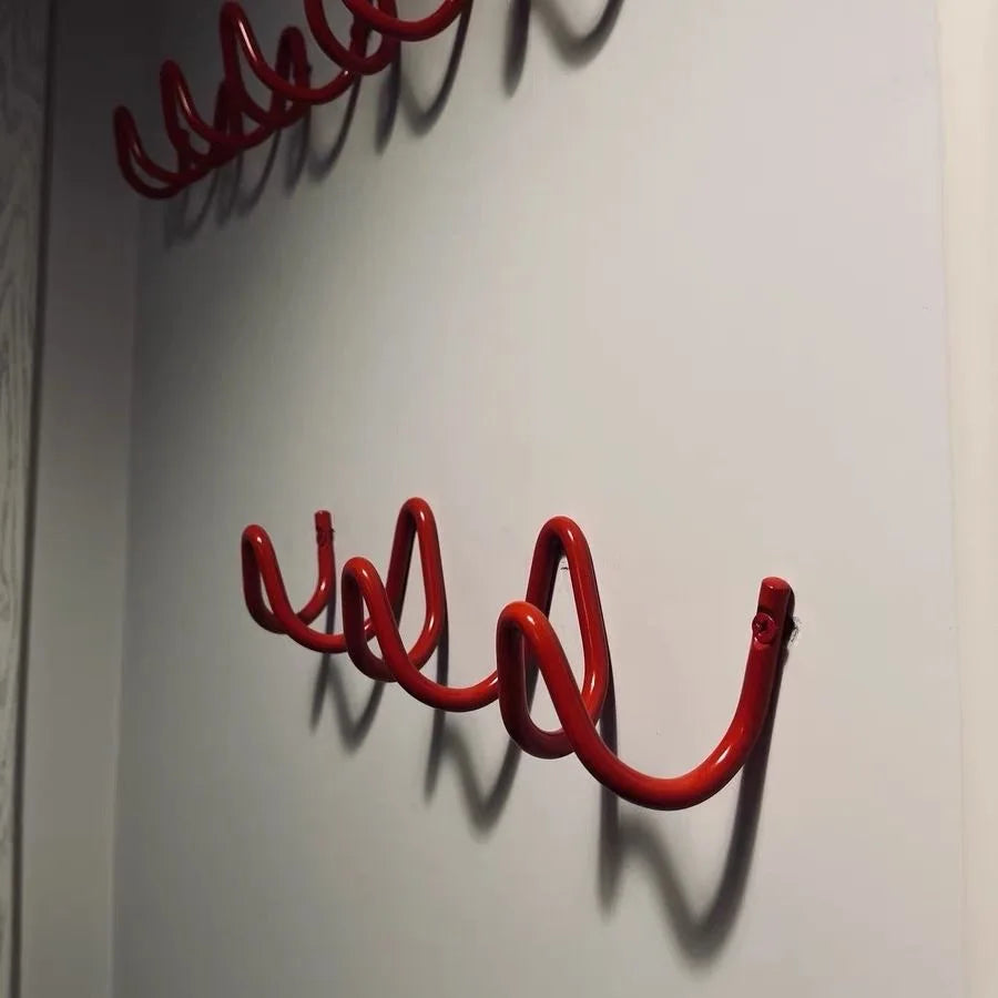 Red wave-shaped wall mounted coat rack with multiple hooks installed on a wall