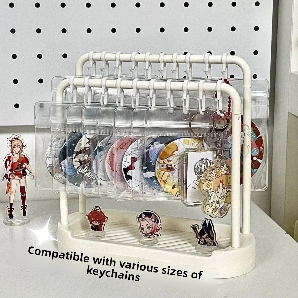 White double-layer desktop display stand organizing badge buttons and keychains in clear pouches with small figures on the base tray