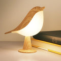 Bird shaped LED touch night light glowing on a table beside books