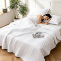 Lightweight quilted summer blanket on a bed, white color, with person sleeping