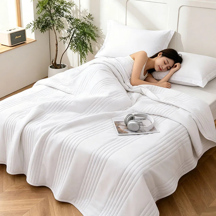 Lightweight quilted summer blanket on a bed, white color, with person sleeping