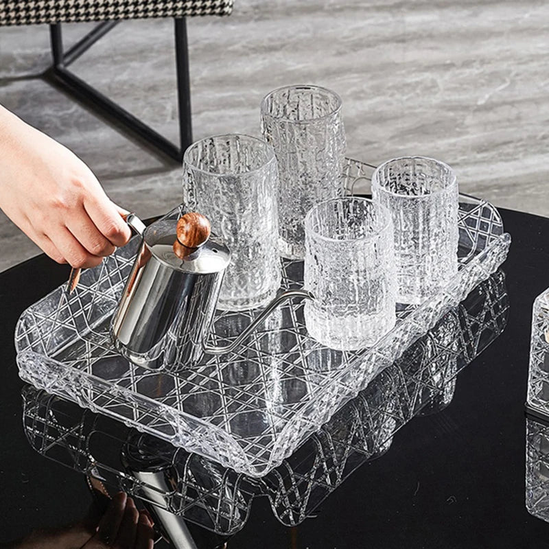 Clear tray holding textured glasses and a small metal teapot on a dark coffee table.