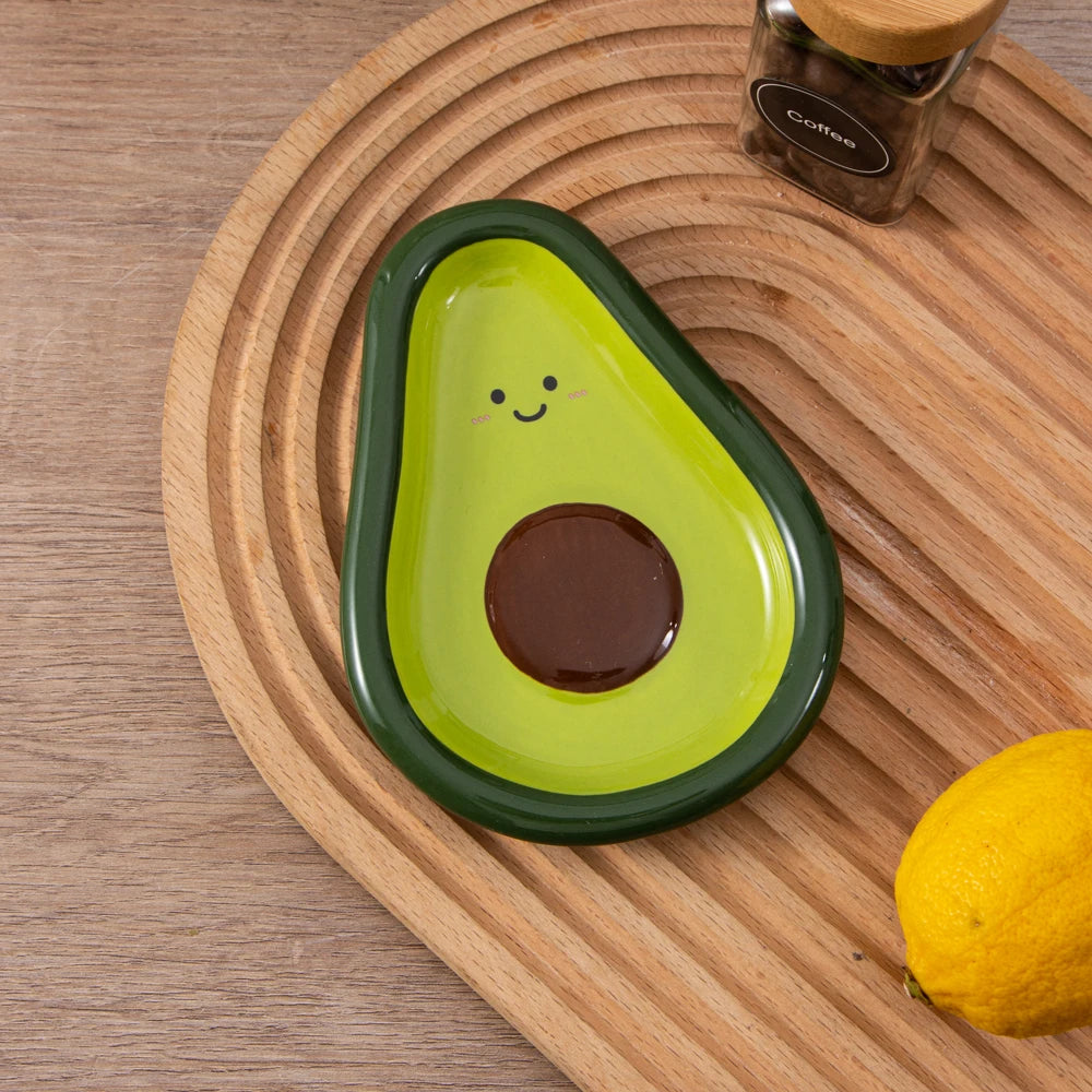 Smiley face avocado ceramic spoon rest styled on a wooden tray with lemon and coffee jar