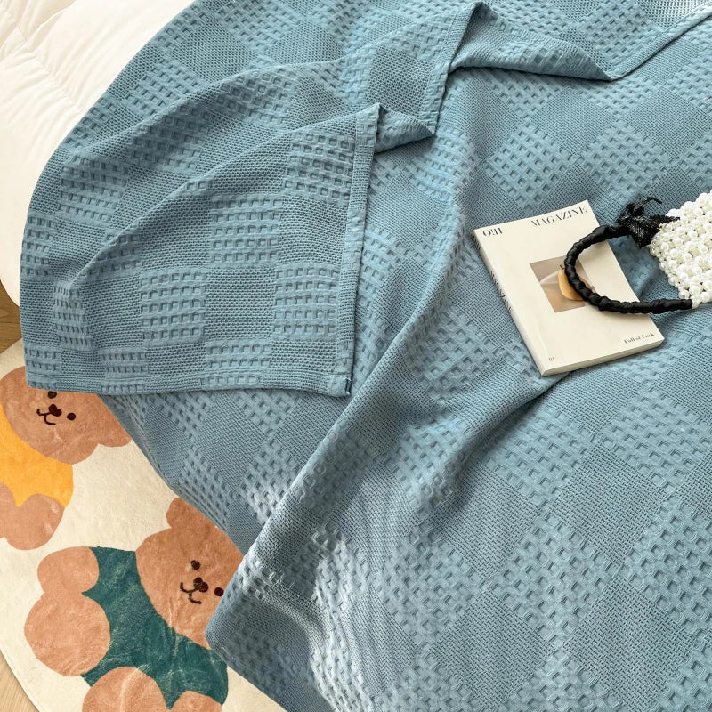Close-up of blue waffle weave throw blanket on bed with magazine and beaded bag